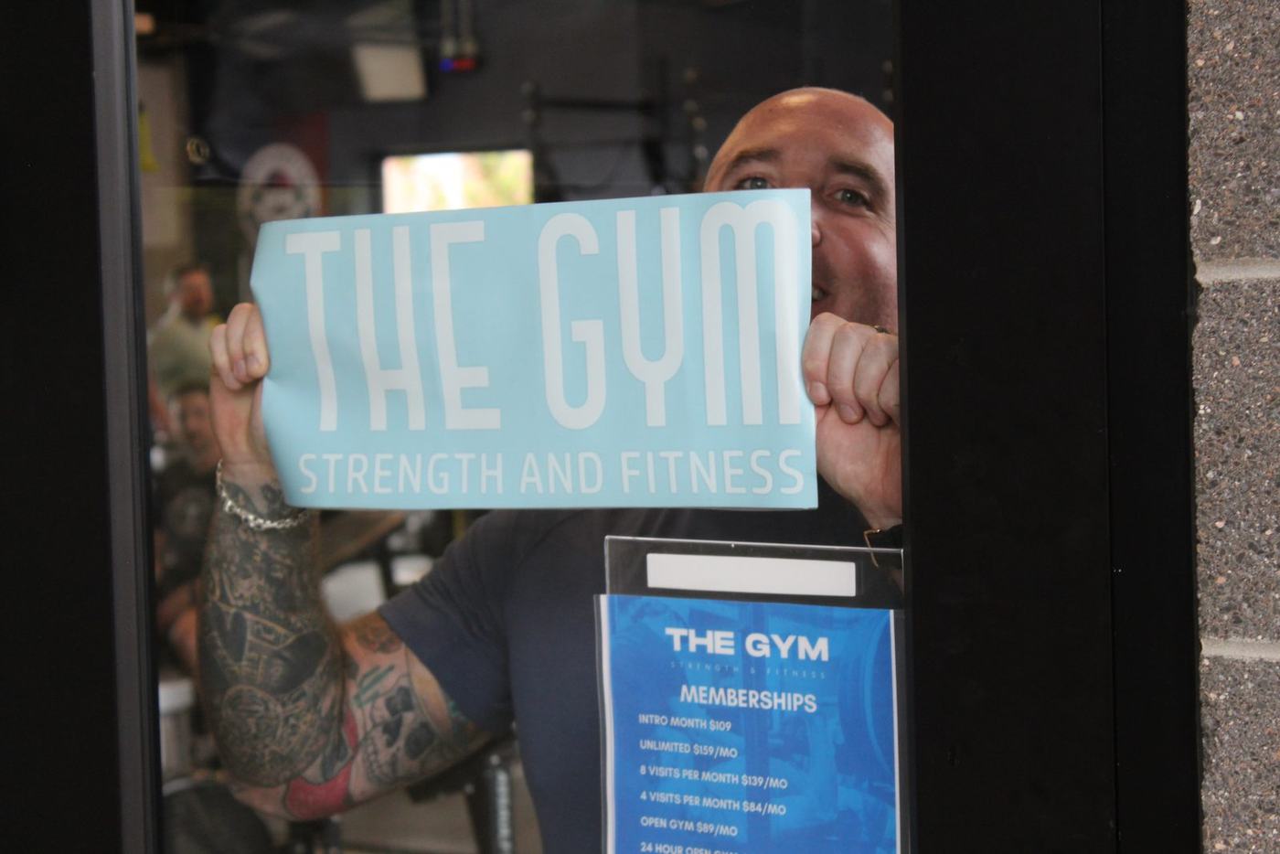 Brandon holding The Gym Strength and Fitness decal in the front window at Revel in Central Park, Denver